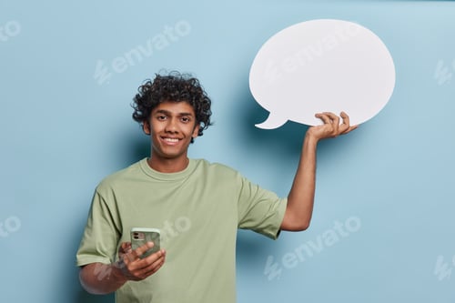 Preview: Glad handsome man with curly hair holds smartphone with chat bubble icon symbolizing communication