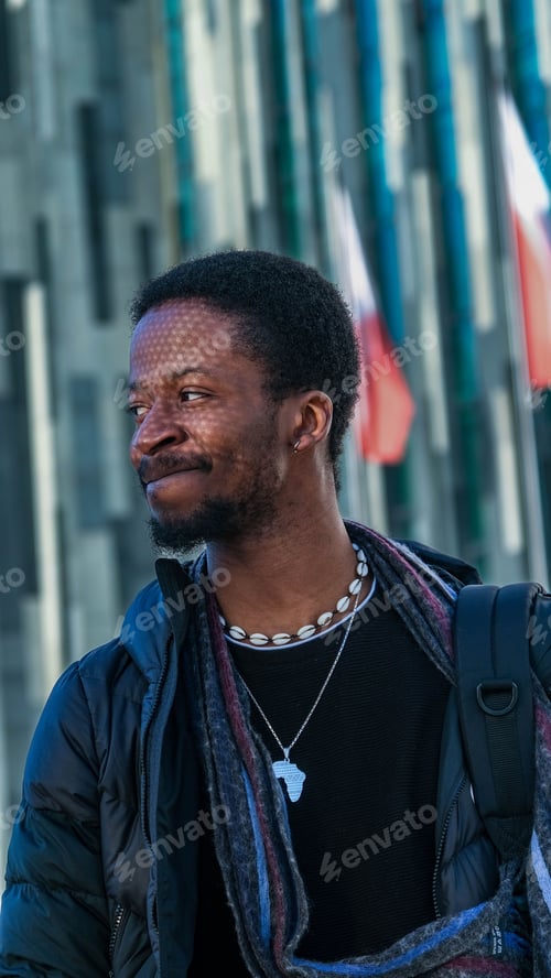 Preview: Young African man in a black outfit walking in a street posing in front of a glass paneled building