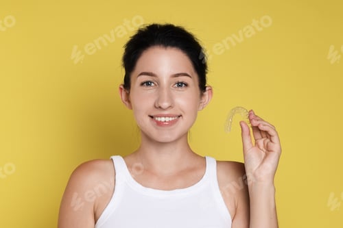 Preview: Portrait of smiling woman with dental aligner on yellow background