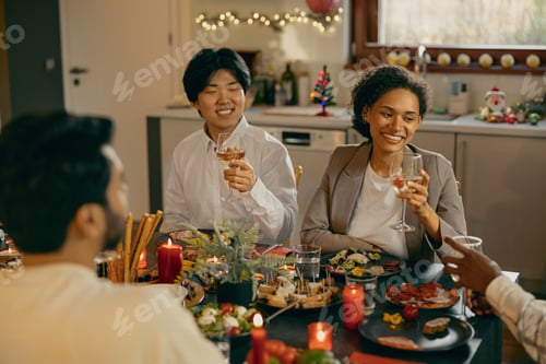 Preview: Happy friends enjoying in conversation and drinking wine during festive dinner at home party