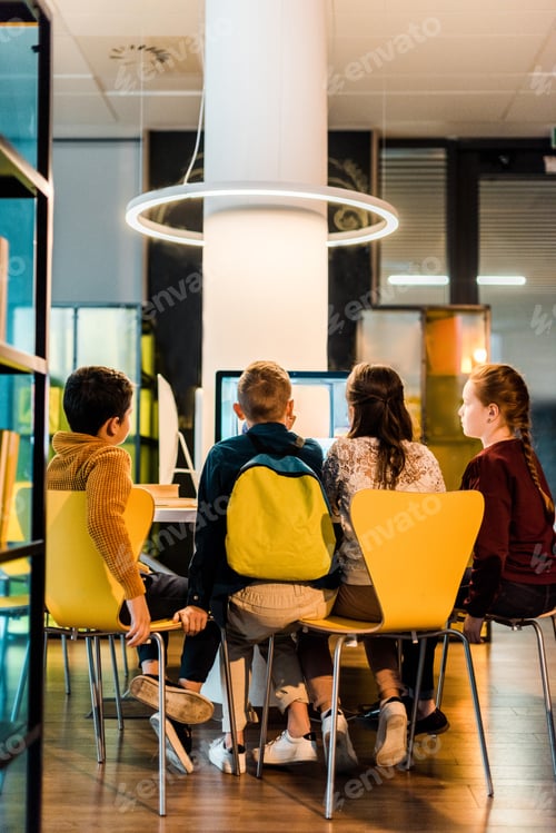 Preview: back view of four schoolkids using computers in modern library