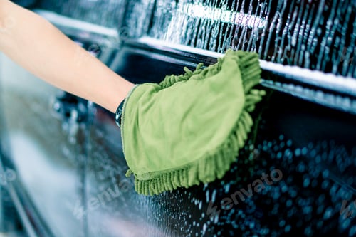 Preview: Close-up of a car wash worker using a green washcloth to wash black luxury car with car wash shampoo