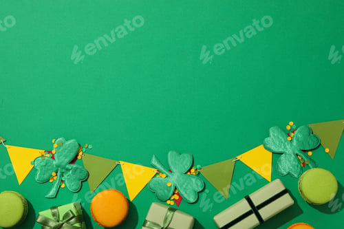 Preview: Clover leaves, paper flags, gift boxes and macaroons on green background, space for text