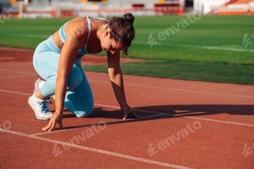 Preview: A fit sportswoman in start position on running track on stadium.