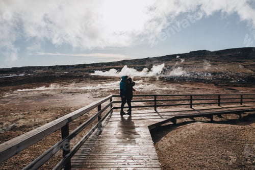 Preview: young couple hugging on wooden walkway near magnificent hot springs in iceland, reykjanes, Gunnuhver