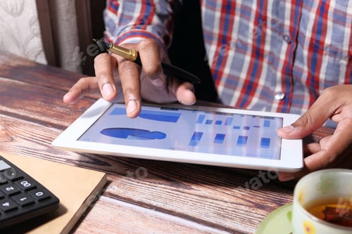 Preview: man's hand working on digital tablet at office desk, using self created chart