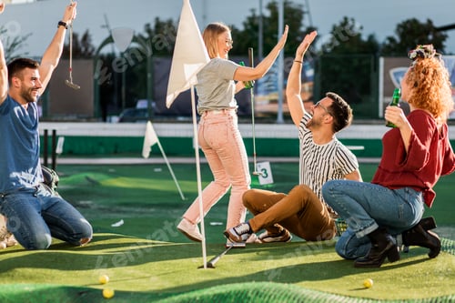 Preview: Group of smiling friends enjoying together playing mini golf in the city.