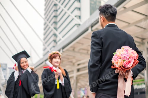 Preview: Businessman hold hiding flower bouquet for congratulation of young woman bachelor's degree graduate
