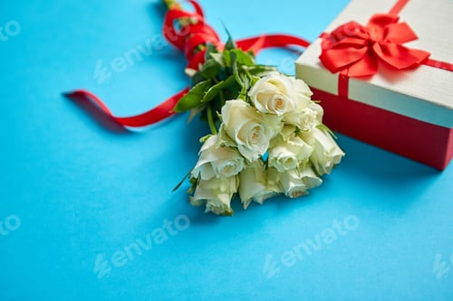 Preview: Bouquet of white roses with red bow on blue background. Boxed gift on side
