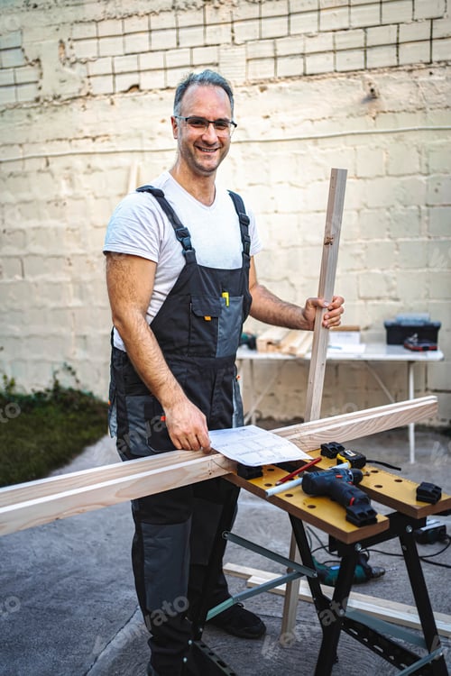 Preview: Mature male carpenter working with wooden plank outdoors