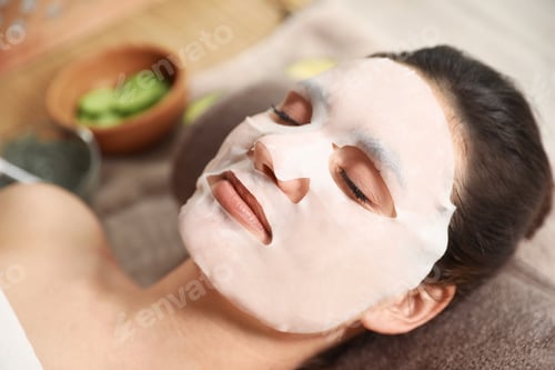 Preview: Beautiful woman with cotton mask sheet on face relaxing in spa salon, closeup