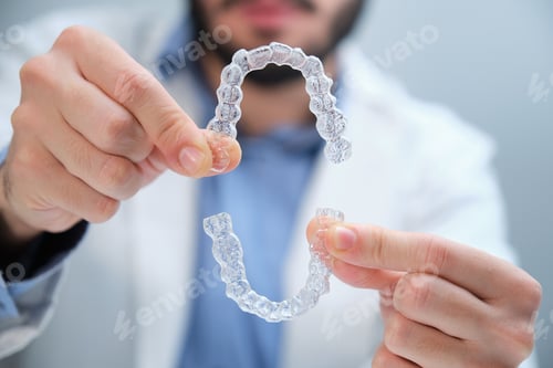 Preview: Unrecognizable orthodontist holding trainer dental braces.