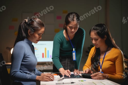 Preview: Three businesswomen are working late in the office, focused on a digital tablet