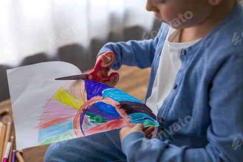 Preview: A young girl carefully cuts out her drawing with scissors, showcasing her creativity and focus.