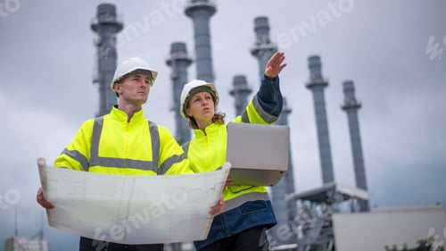 Preview: Engineers wearing safety gear, including hard hats examining survey a standing industrial facility g