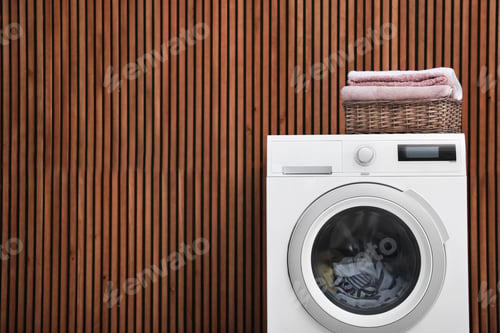 Preview: Washing machine and laundry basket with towels near wooden wall. Space for text