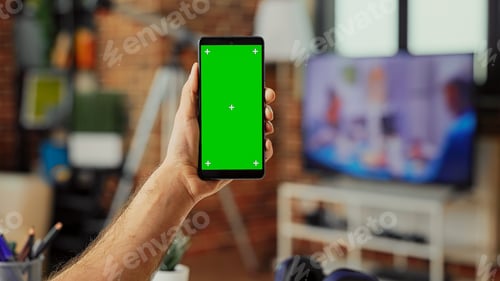 Preview: Male freelancer holding smartphone with green screen display