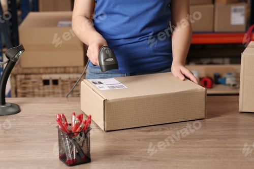 Preview: Post office worker with scanner reading parcel barcode at counter, closeup