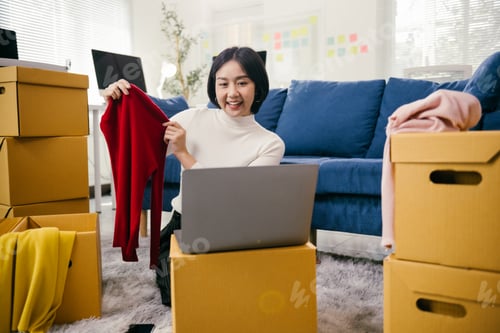 Preview: Asian female entrepreneur showing clothes in a live stream from home