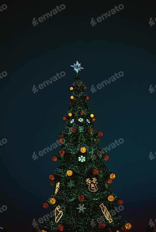 Preview: Decorated evergreen tree with colorful lights and ornaments at night, topped with a bright star.