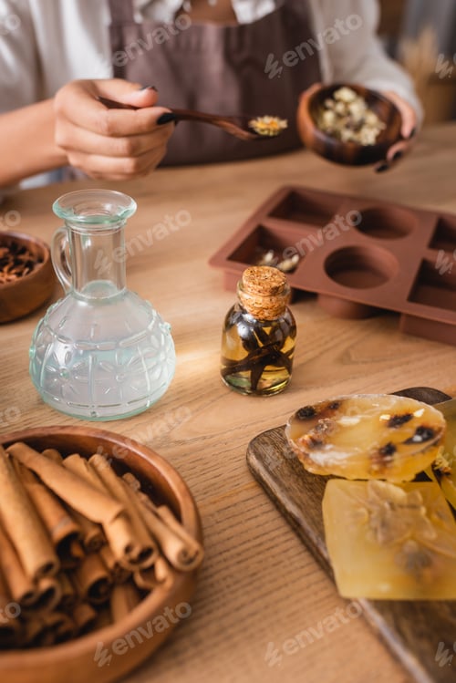 Visualização: vista recortada de uma artesã afro-americana embaçada segurando ervas secas perto de sabonete artesanal e