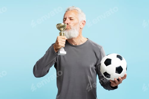 Preview: Bearded mature man, football played holding ball, kissing trophy cup, celebration success isolated