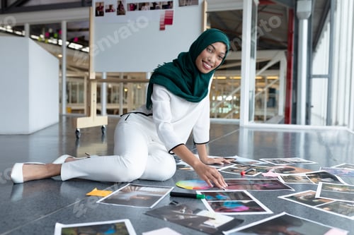 Preview: Woman wearing green hijab kneeling and arranging photographs and swatches on modern studio floor