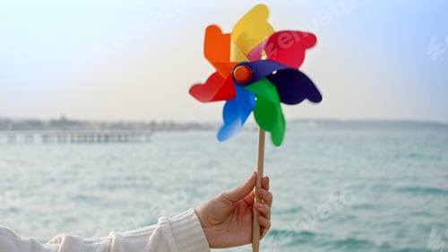 Preview: Young woman playing with a colorful spinning pinwheel on the sandy sea beach. Summer holiday, travel