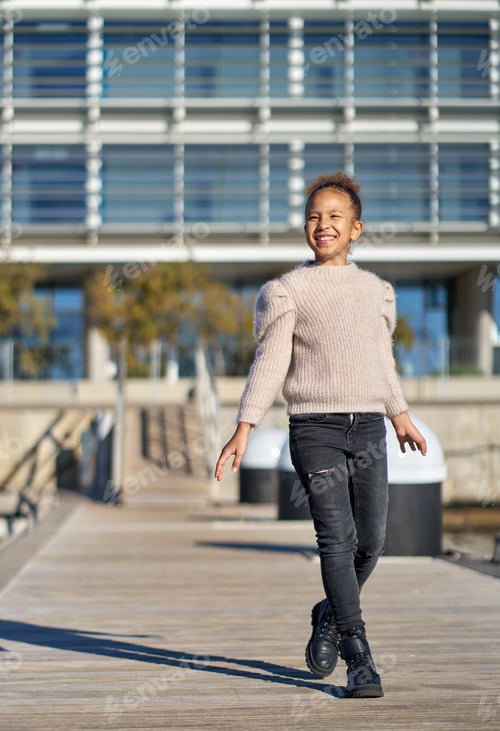 Preview: Smiling girl walking on pier with modern building in background