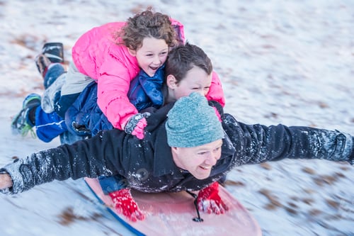 Preview: Portrait of father, son and daughter laying on top of each other riding sledge down hill