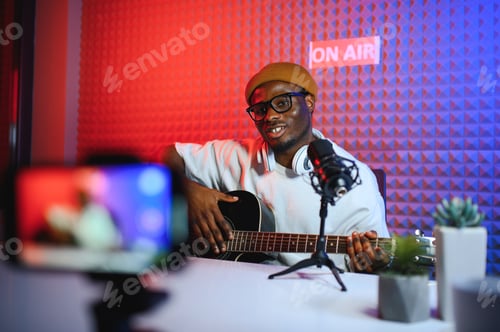 Preview: A young stylish music teacher playing guitar in front of smartphone camera.