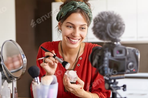 Preview: Cheerful teenage girl recording video tutorial at home, looking at camera fixed on tripod, sitting a