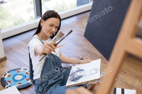 Preview: Pretty painter posing on camera with canvas and paintbrushes
