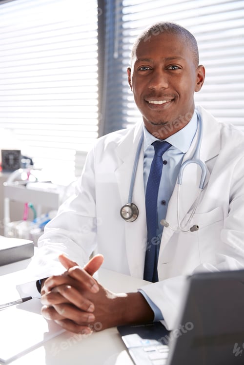 Preview: Portrait Of Smiling Male Doctor Wearing White Coat With Stethoscope Sitting Behind Desk In Office