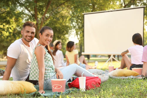 Preview: Young couple with popcorn watching movie in open air cinema. Space for text