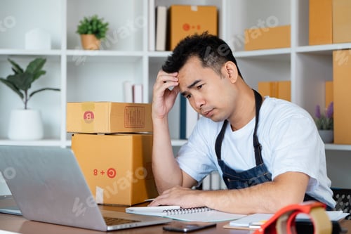 Preview: Frustrated small business owner managing orders at home office with cardboard boxes