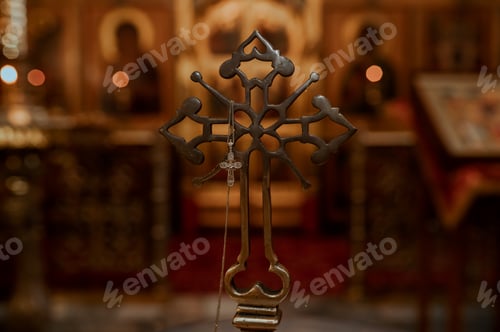 Preview: Small Golden Orthodox Cross Pendant with White String Near a Large Metallic Crucifix in Church
