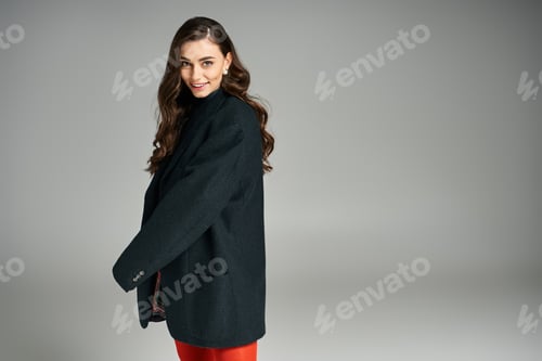 Preview: Elegant young woman poses in stylish coat against soft gray backdrop