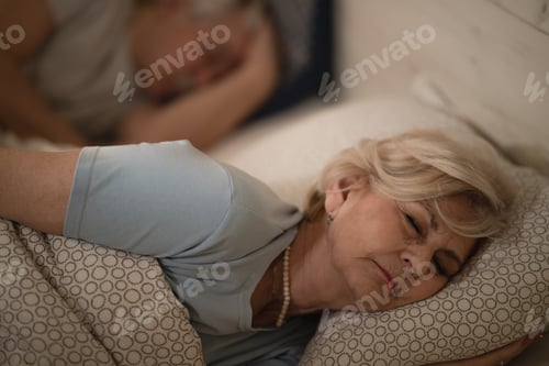 Preview: Tired mature woman sleeping in bed at night.