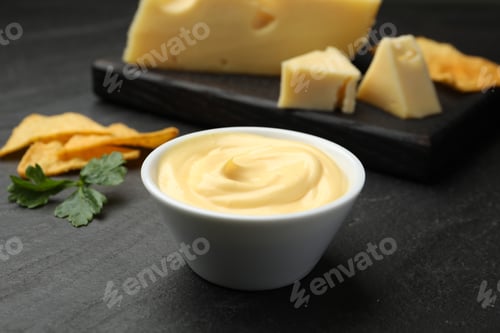 Preview: Tasty dipping cheese sauce in bowl, nacho chips and parsley on black table, closeup