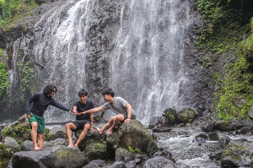 Preview: Three Young Friends Stacking Hands While Sitting On Rock Near Waterfall