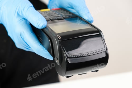Preview: Close up woman in rubber gloves holding a pos terminal. Contactless payment during pandemic using