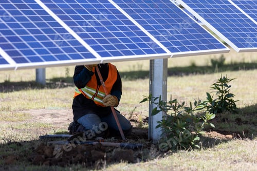 Preview: Worker in a safety vest installing solar panels, photovoltaic modules in a field