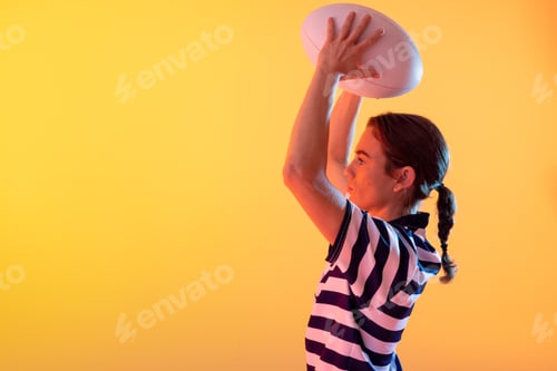 Vista previa: Caucasian female rugby player with rugby ball over neon yellow lighting