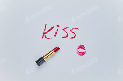 Preview: Text KISS drawing and trace of kiss by red lipstick on white sheet. Sketch closeup on white backdrop