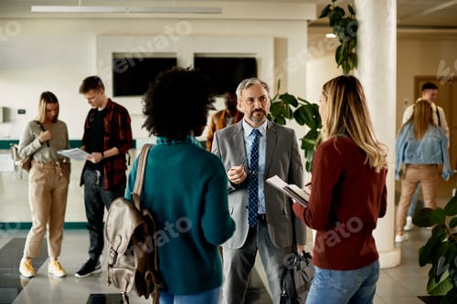 Preview: Mature professor talking to female students at university hallway.