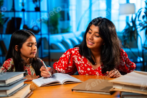 Preview: Elder Indian girl helping younger sister with homework at study table in home environment