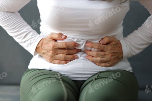 Preview: Senior woman sitting on the sofa in the house is sick and has a stomach ache.