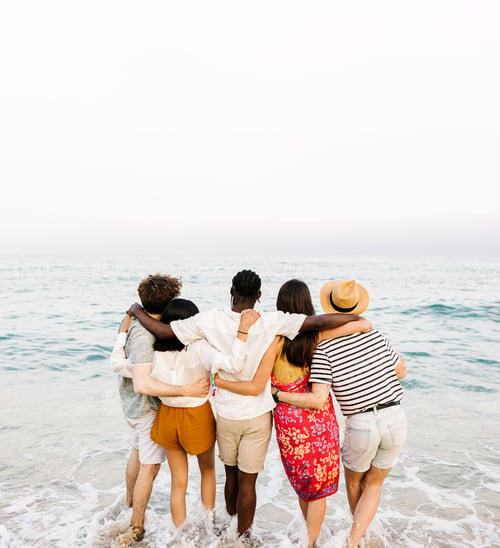 Preview: Rear view of young friends hugging each other in front of the sea