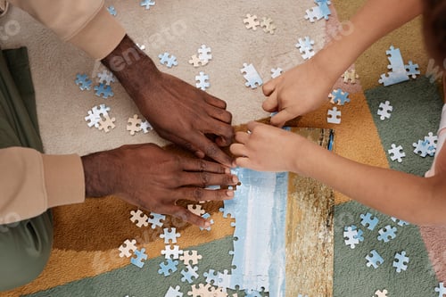 Preview: Top view father and kid solving jigsaw puzzle on floor at home, focus on hands holding pieces